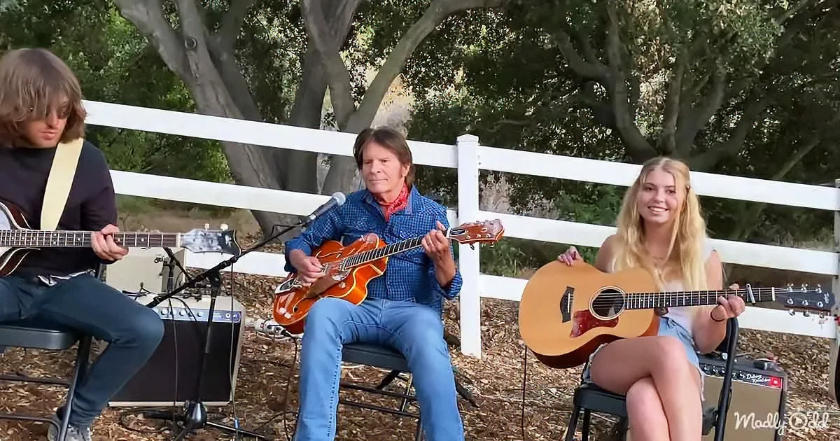 A man in a blue shirt plays a guitar while a woman in a white top holds an acoustic guitar, both seated outdoors.