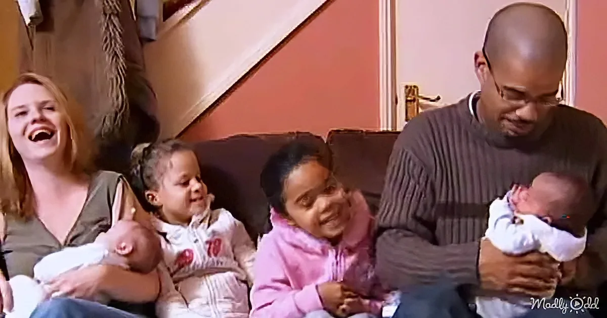 A family of five, including two adults and three children, sits together on a couch, smiling and laughing.