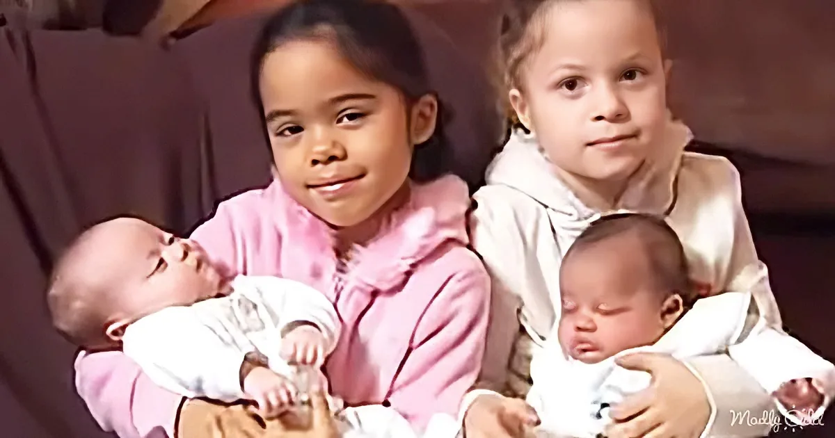 Two young girls hold newborn babies, one in pink and the other in white, both smiling.