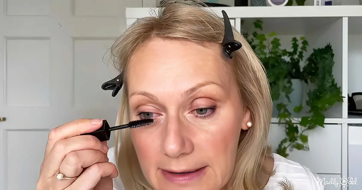 A woman applies mascara with a clip-on eyelash curler, focusing on her eye.