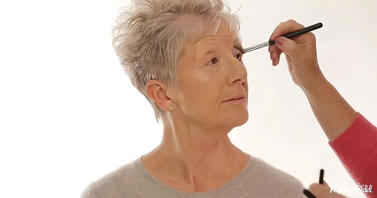 An older woman with short gray hair is having makeup applied to her eye.