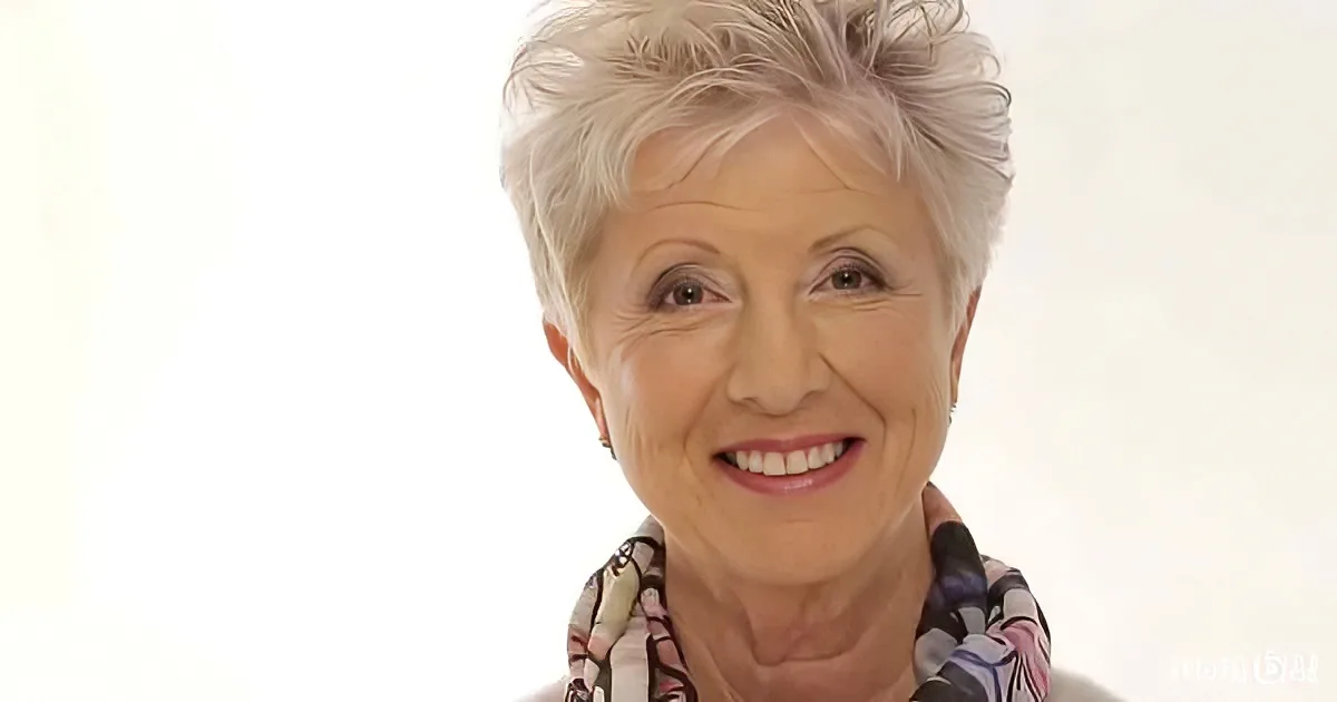 A smiling older woman with short white hair, wearing a colorful scarf, against a plain white background.