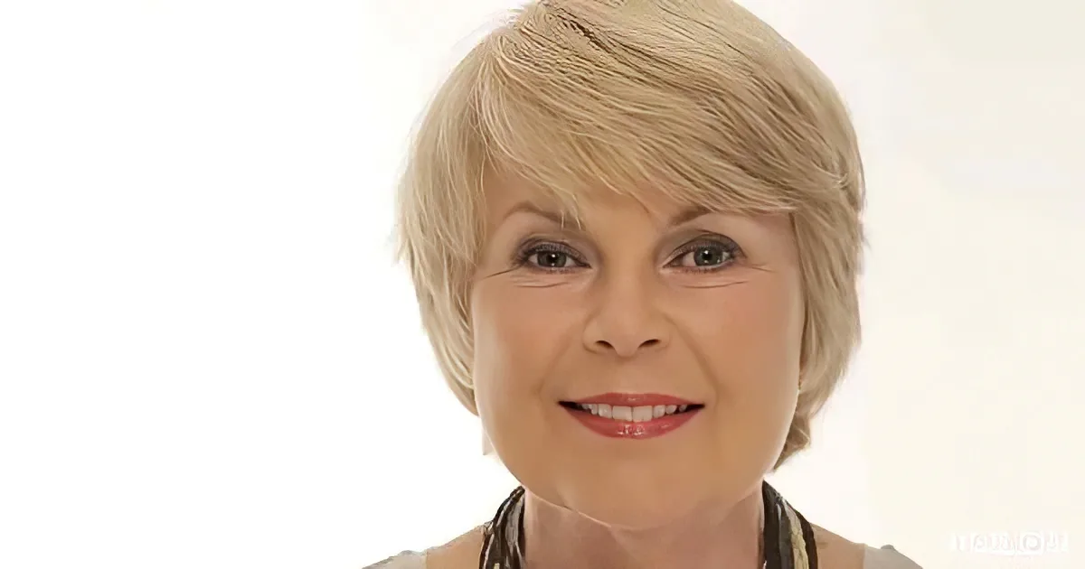 A woman with short, blonde hair and a warm smile, wearing a patterned top.