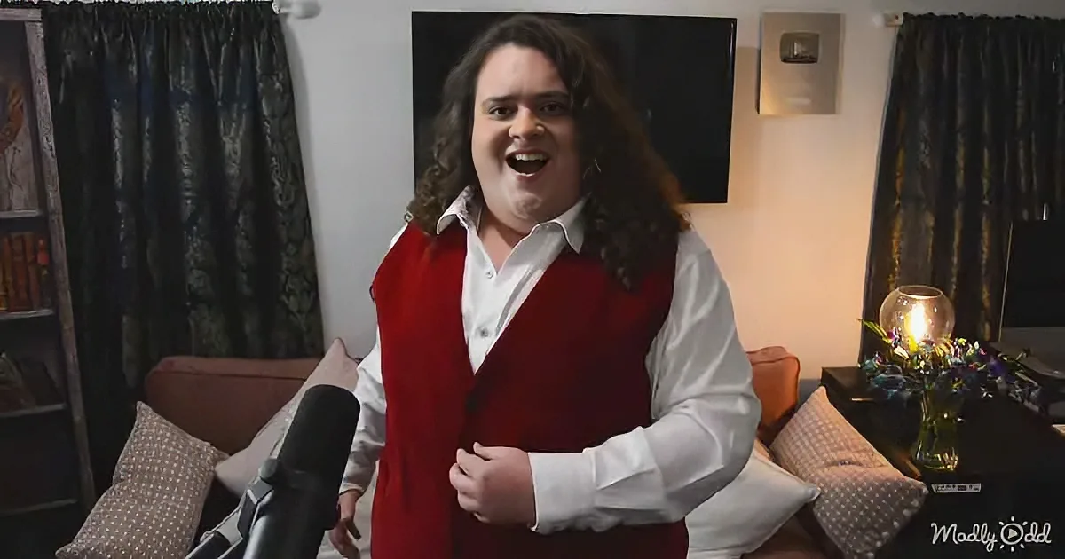 A person in a red vest and white shirt stands in a room with a microphone, smiling widely.