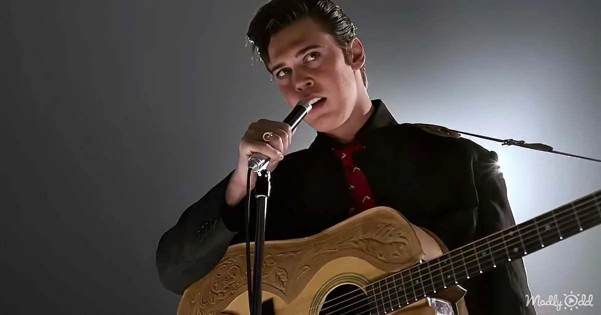 A man in a black suit and red tie sings into a microphone while playing a guitar with ornate details.