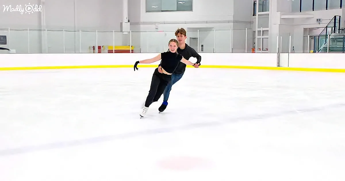 A couple ice skating together, the woman leading with a smile, both wearing black.