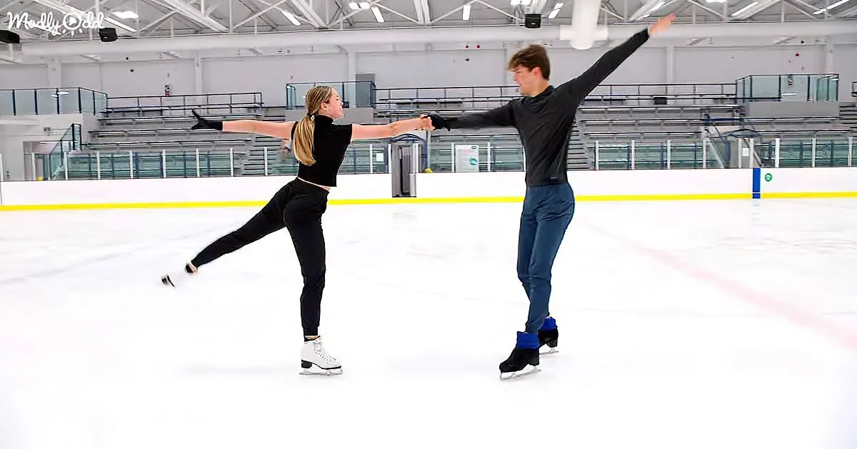 Two figure skaters in black attire perform a synchronized move on an indoor ice rink.