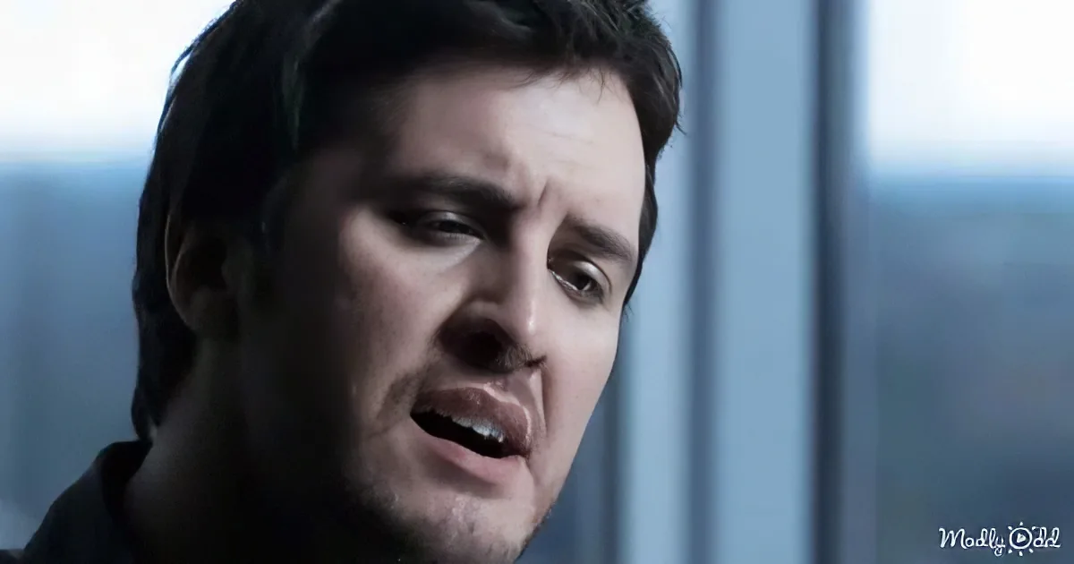 A man with dark hair and a serious expression is shown in a close-up shot.