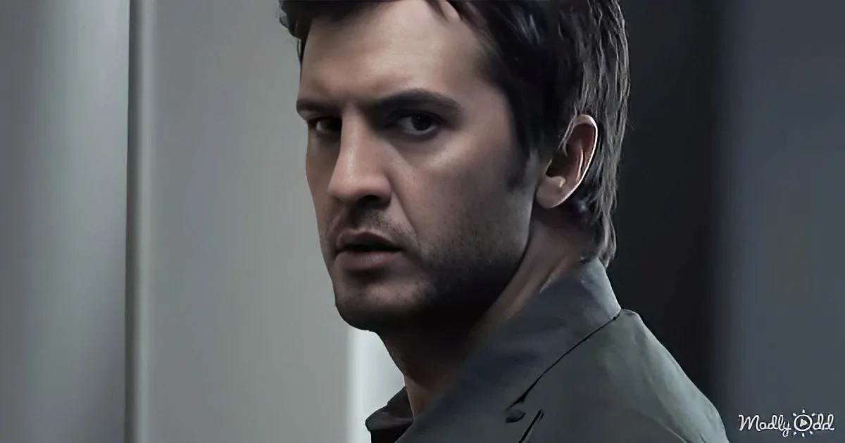 A man with short dark hair and a beard, wearing a dark jacket, looks off to the side with a serious expression.