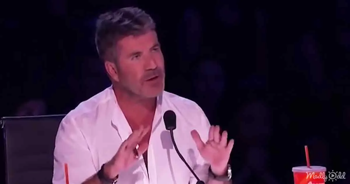 A man in a white shirt is gesturing with his hands while speaking into a microphone.