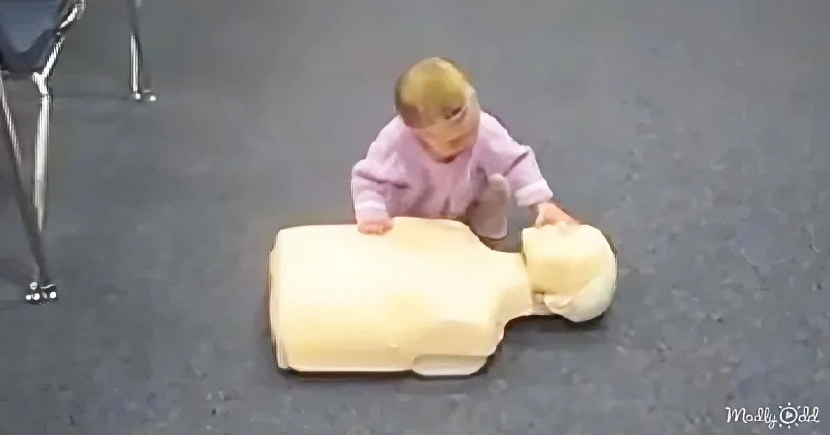 A baby in a pink outfit is interacting with a large, light-colored object on the floor.