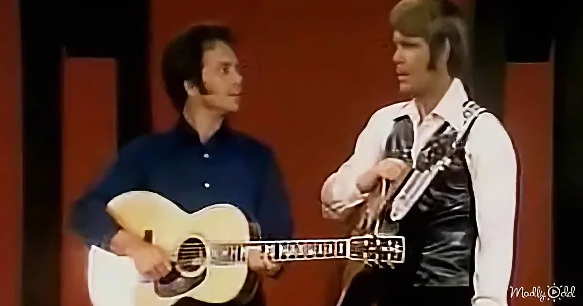Two men, one in blue shirt playing guitar, the other in white shirt and black vest, both holding guitars.