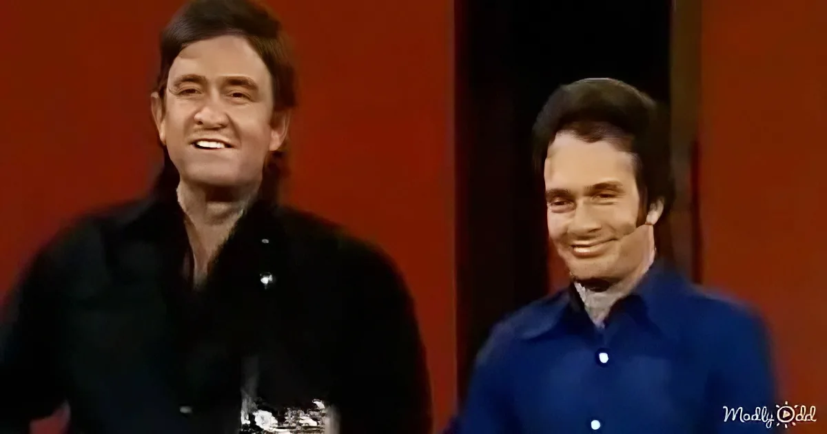 Two men in vintage attire smile on a stage with a red backdrop.