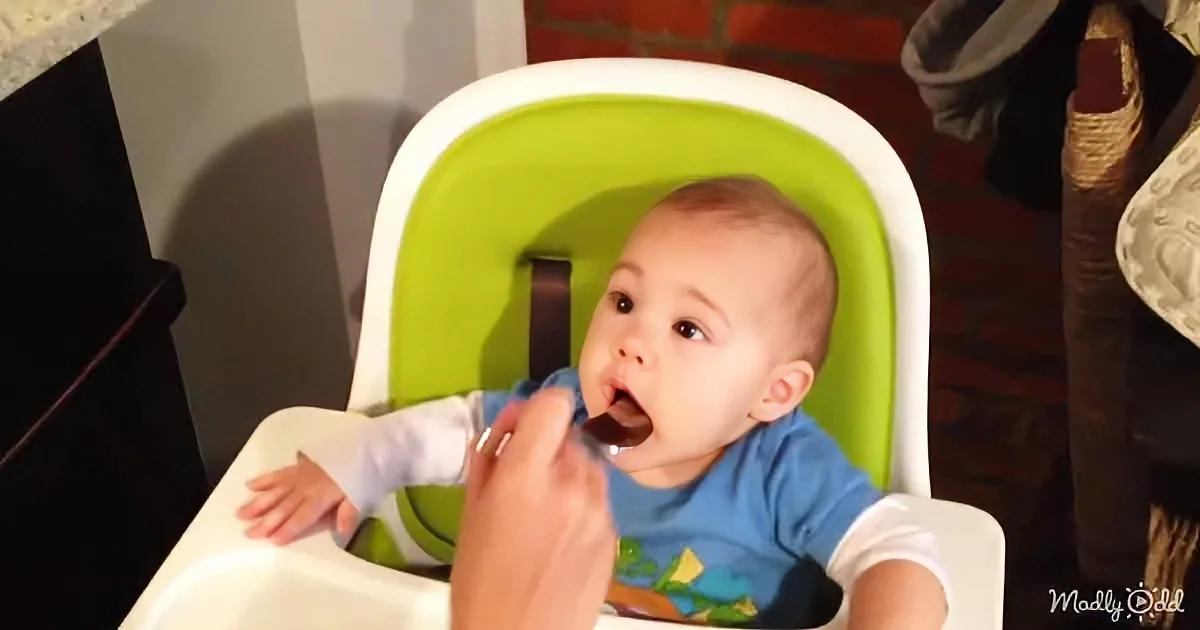 A baby in a high chair being fed by a hand holding a spoon.