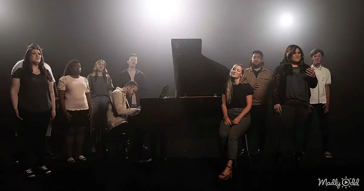 A group of people stands around a piano, with one person seated at the piano and another in front, possibly singing or...