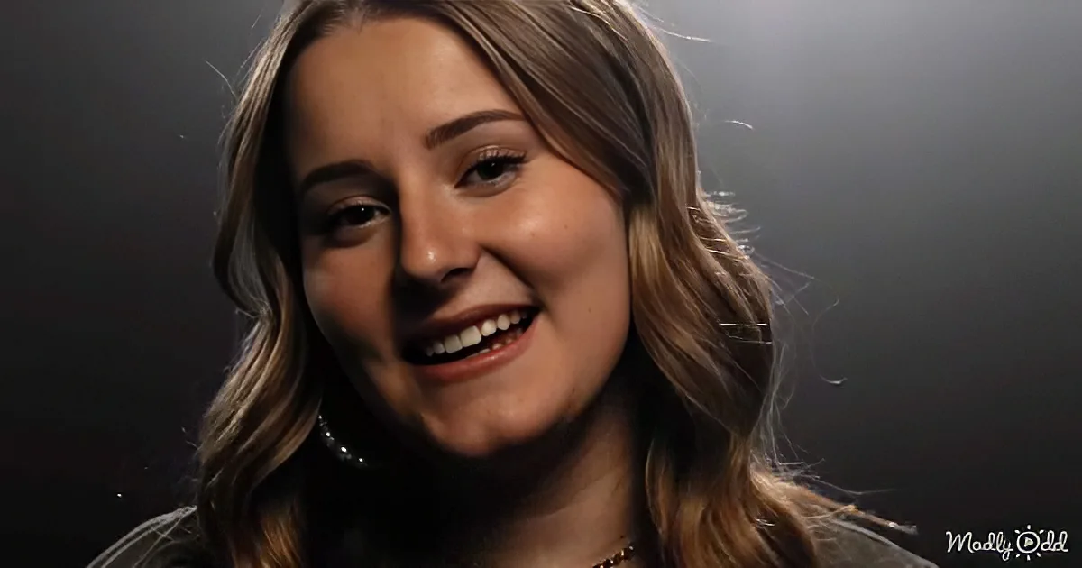 A smiling woman with long, wavy brown hair and a necklace, set against a dark background.