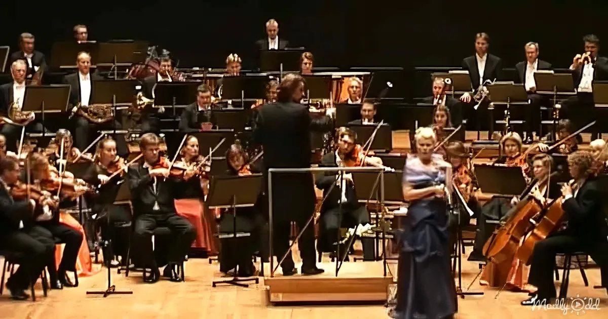 Conductor leads orchestra with a woman in blue dress singing in front.