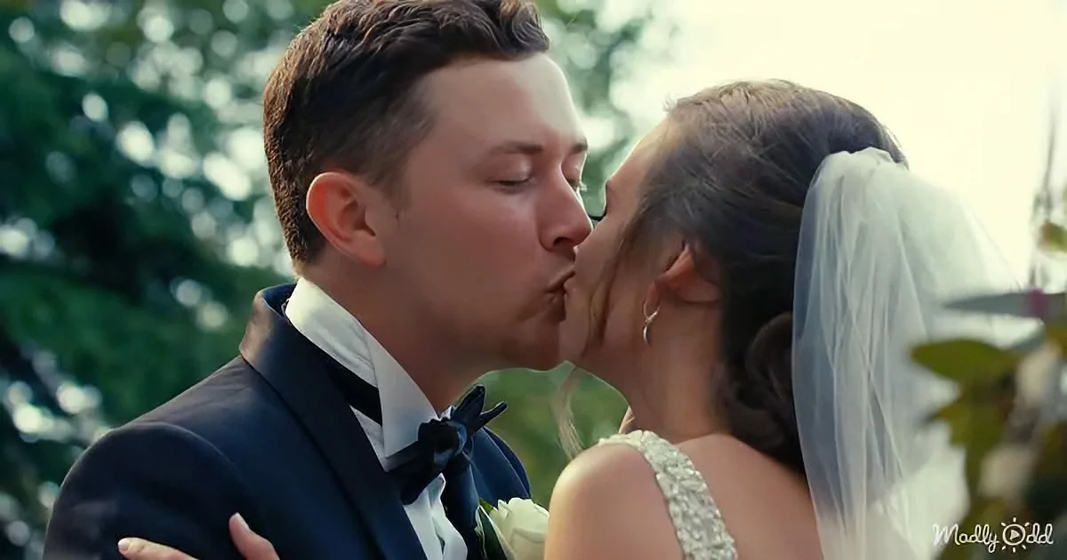 A bride and groom share a kiss, the bride in white, the groom in a tuxedo.