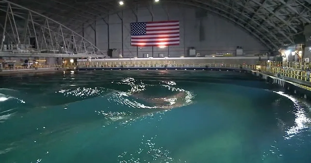 A large, circular, rippling wave in a pool with an American flag hanging in the background.