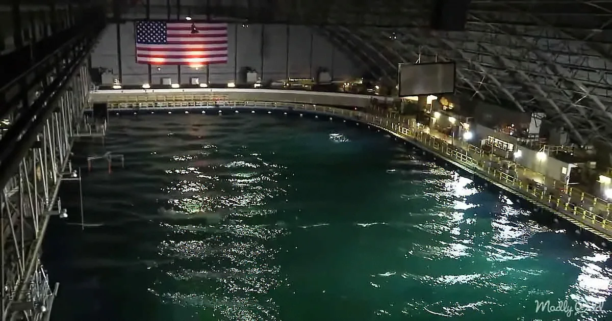 A large, green, indoor pool with a U.S. flag hanging above and metal railings on both sides.