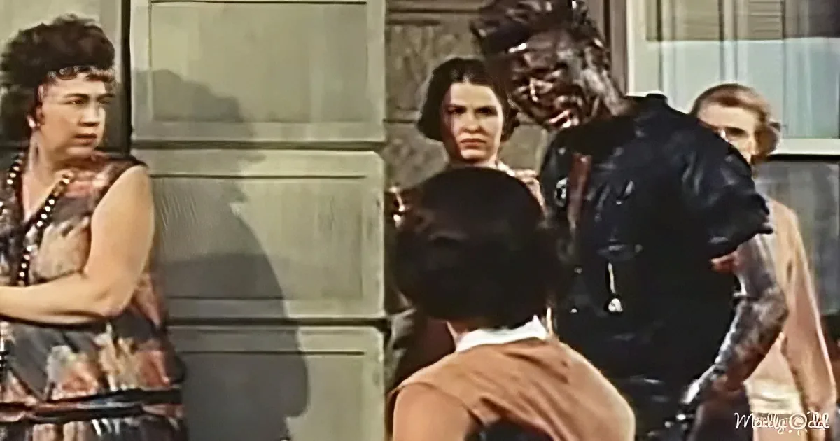 A person in a black leather outfit is being restrained by another individual in a brown outfit, with others observing in...