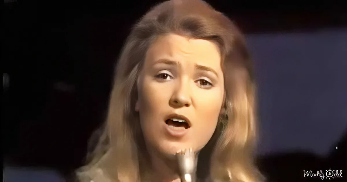 A woman with long blonde hair sings into a microphone, her expression intense.