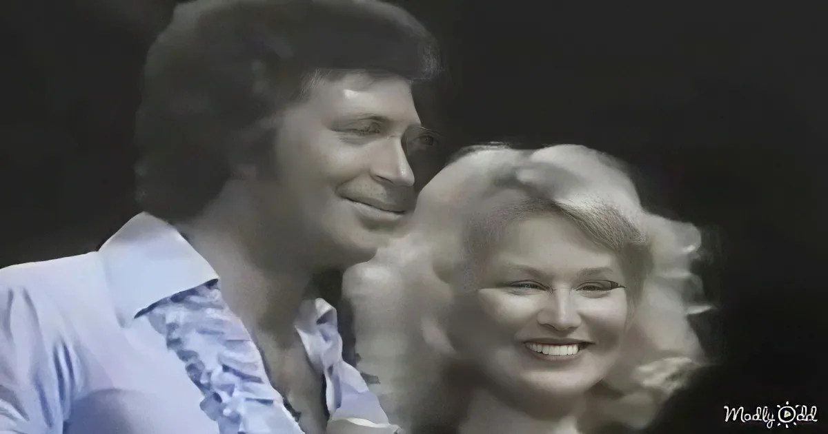 A man in a light blue shirt and a woman with blonde hair are smiling together.