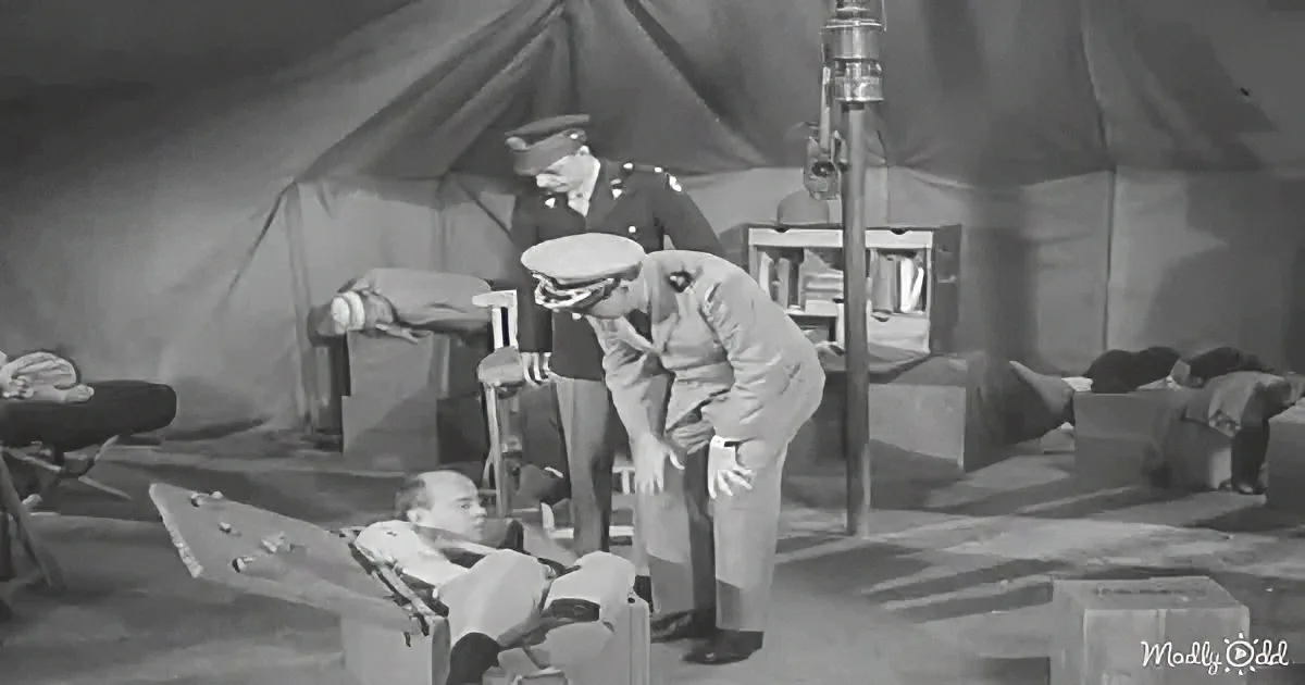 A soldier in uniform bends over another soldier lying on a stretcher in a tented area.