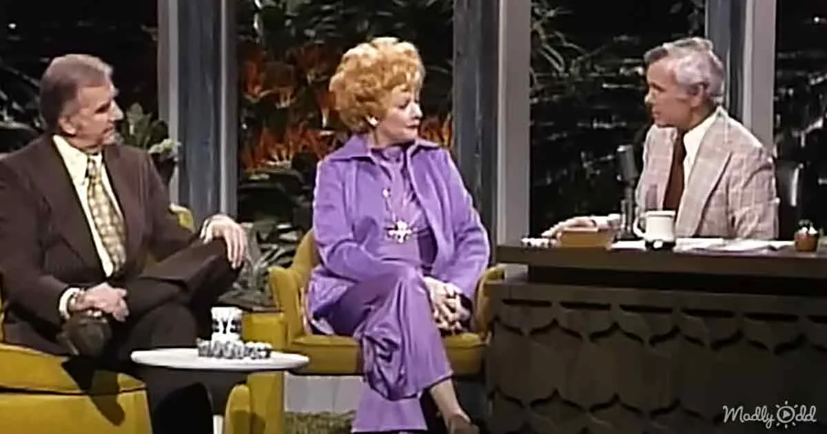 A woman in a purple outfit sits on a yellow chair, engaging in conversation with a man in a suit.