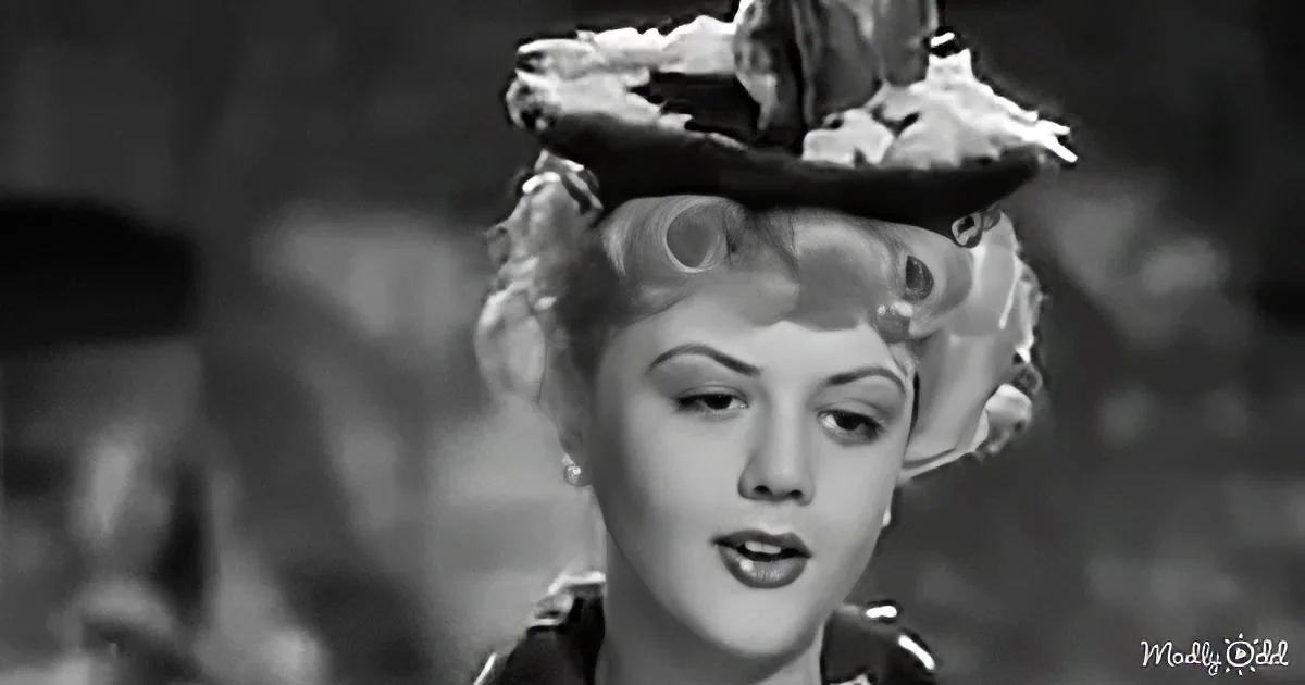 A woman with curly hair and a floral hat is singing into a microphone.
