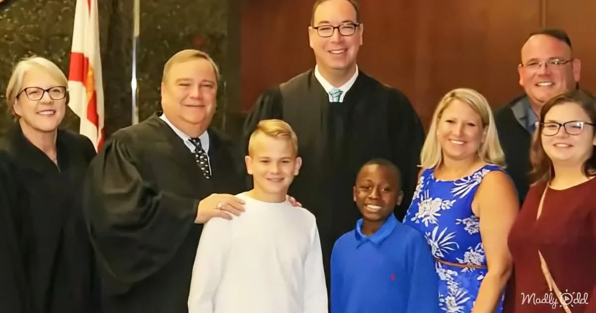 A group of people, including a judge and two children, pose for a photo in a courtroom setting.