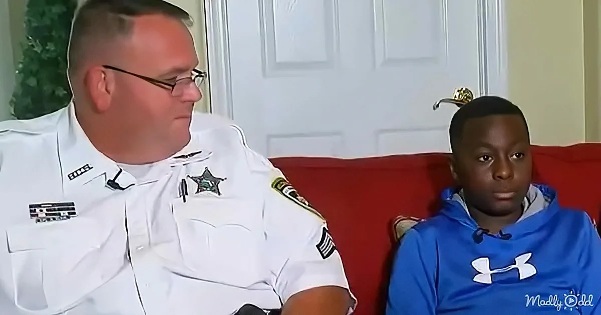 A man in a sheriff's uniform sits on a red couch, talking to a young boy in a blue hoodie.