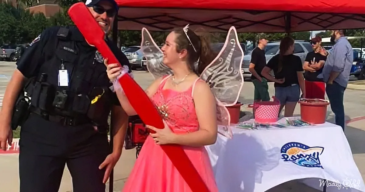A girl in a fairy costume holds a red wand, interacting with a police officer at a community event.