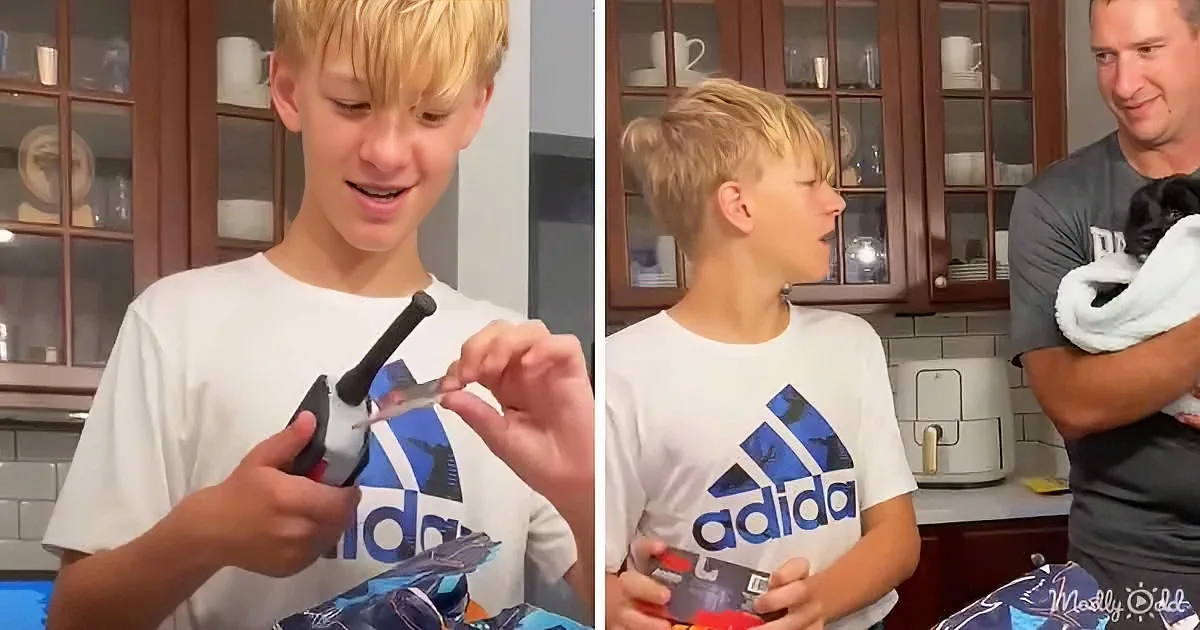A boy in an Adidas shirt is opening a toy package with a smile, while a man holds a dog nearby.