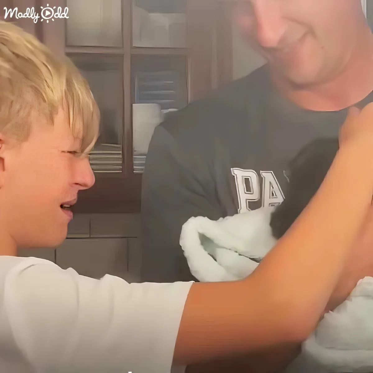 A young boy in a white shirt is interacting with an adult in a dark shirt, both in a home setting.