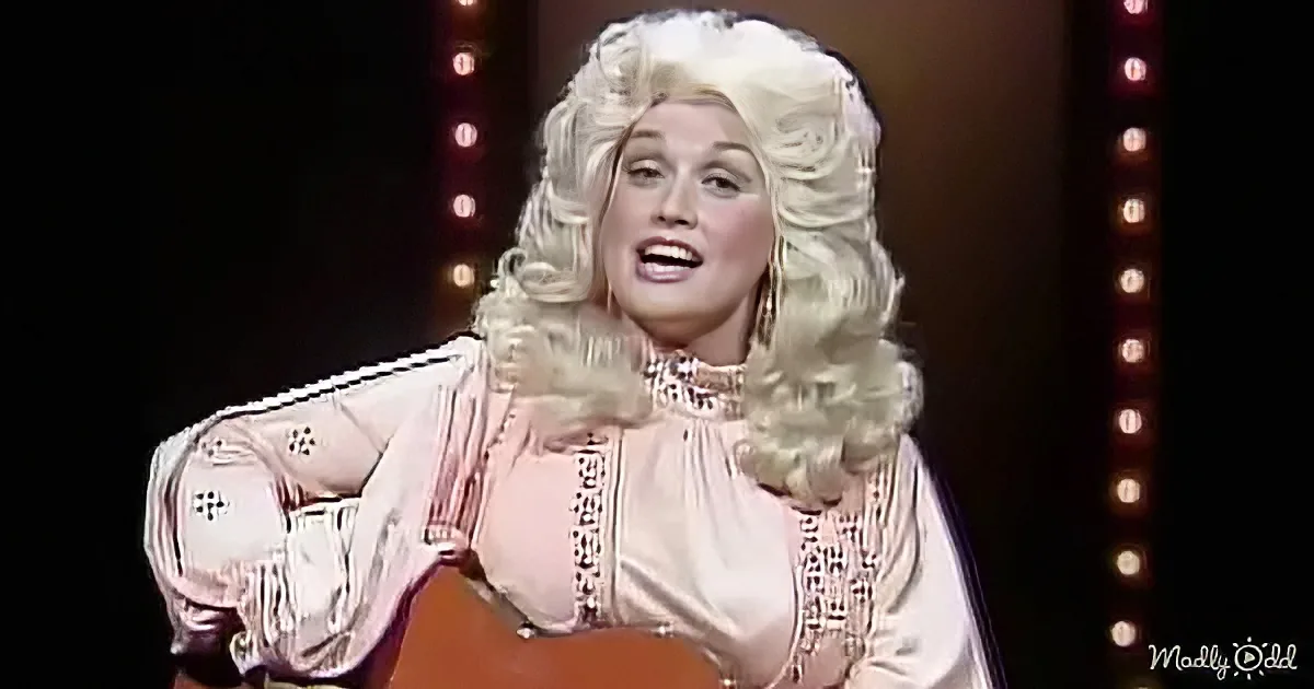 A person with voluminous blonde hair and a pink outfit is holding a guitar and singing.