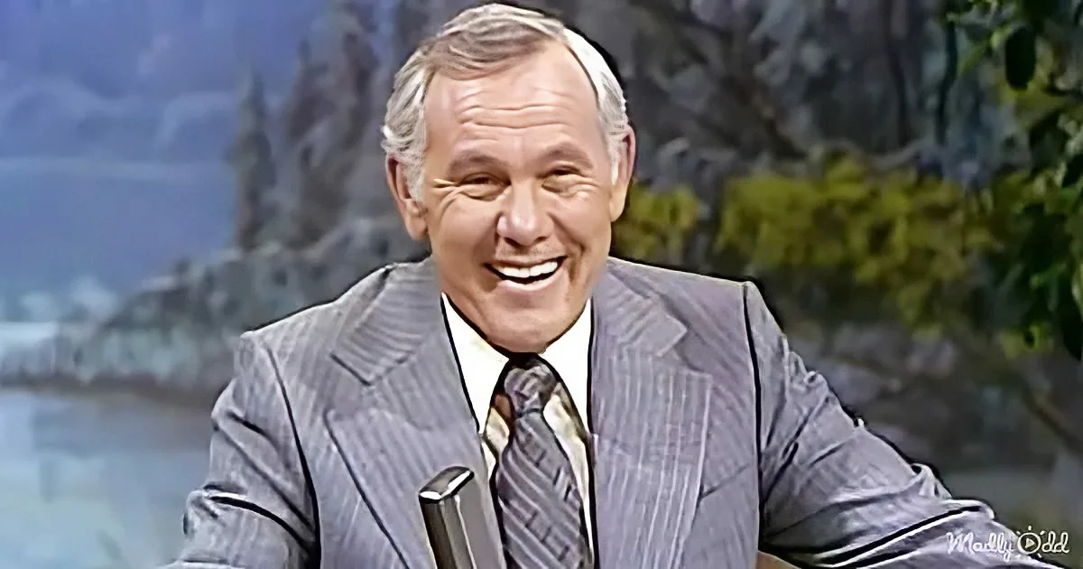 A man in a pinstripe suit and striped tie smiles while holding a microphone, with a scenic background.