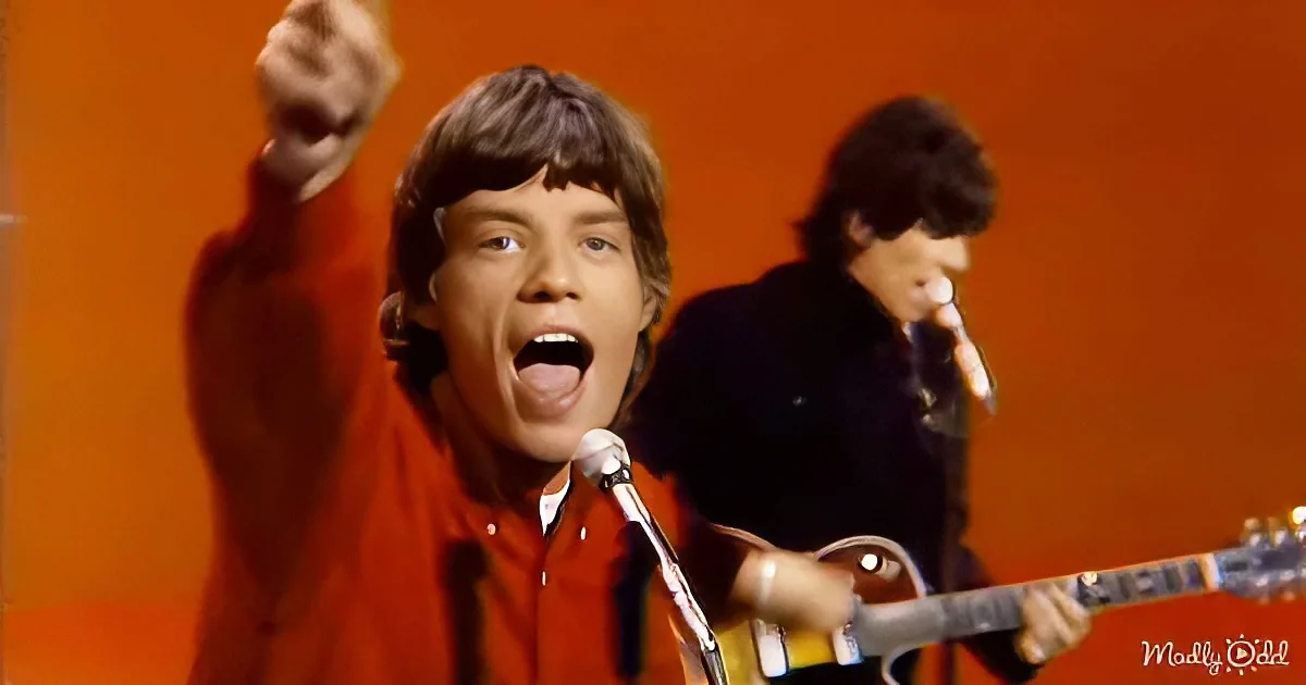 A man in a red shirt sings passionately into a microphone, raising his fist in the air.