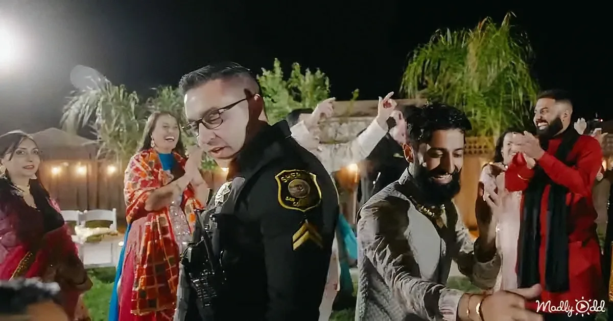A man in a police uniform stands amidst a group of people at a nighttime outdoor gathering.