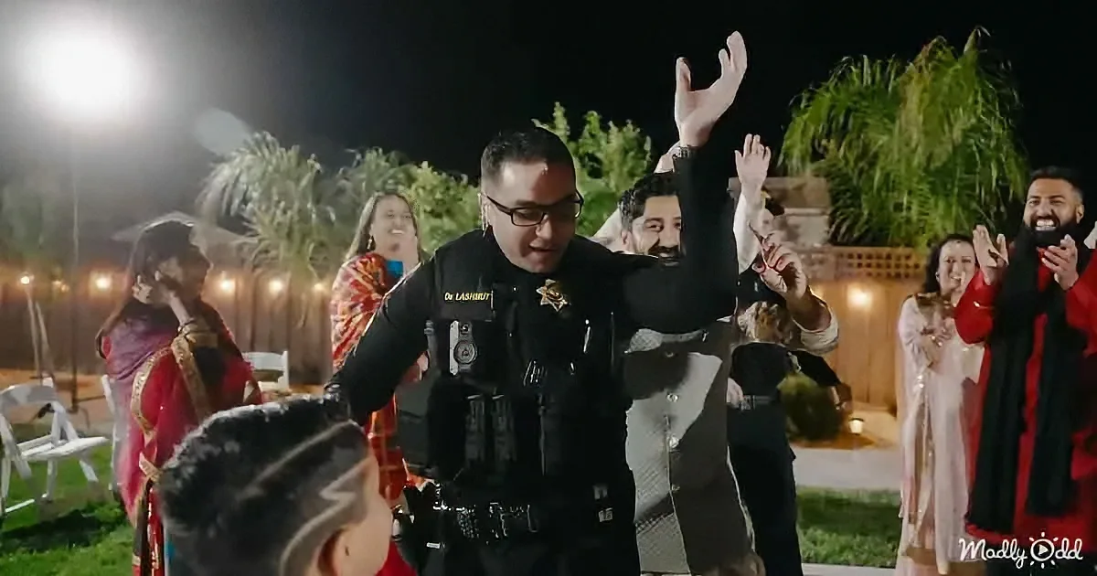 A police officer in uniform dances energetically at a nighttime outdoor event, surrounded by people.
