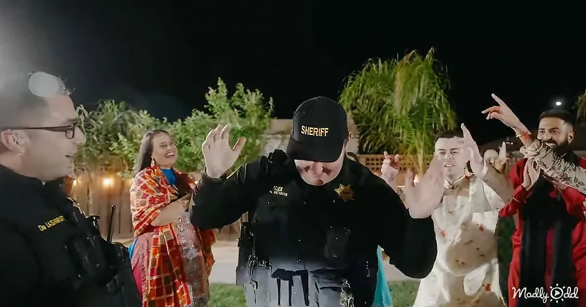 A sheriff in uniform gestures while surrounded by people in colorful attire, with palm trees and night sky in the background.