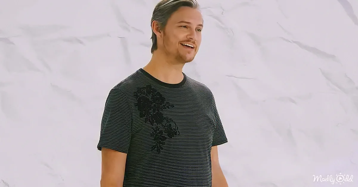 A man with a beard and striped shirt smiles against a crumpled white background.