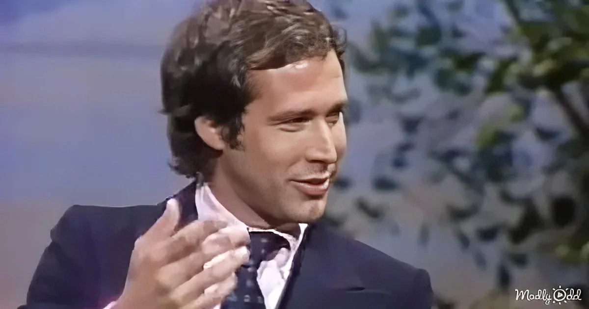 A man in a suit and tie is gesturing with his right hand, appearing to speak or explain something.