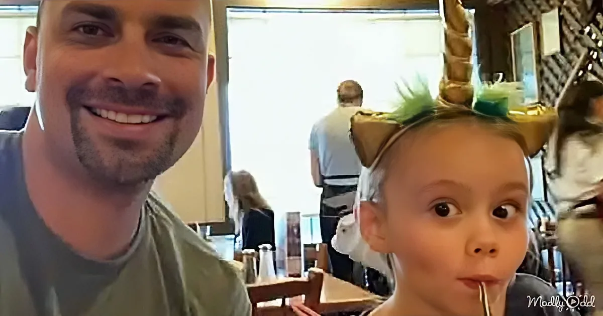 A man and a child with a unicorn headband smile in a restaurant setting.