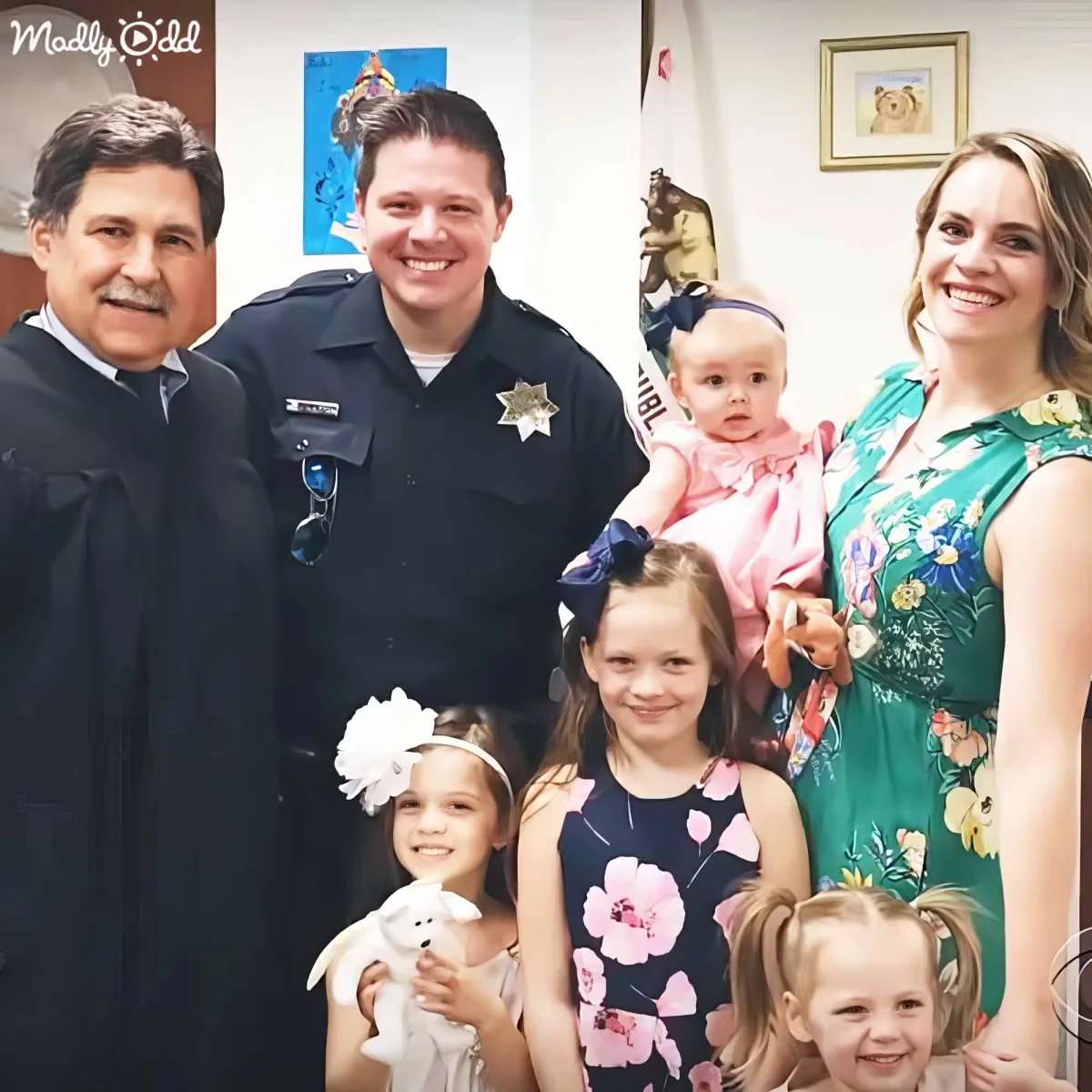 A police officer stands with a family, including a baby and two young girls, in a formal setting.