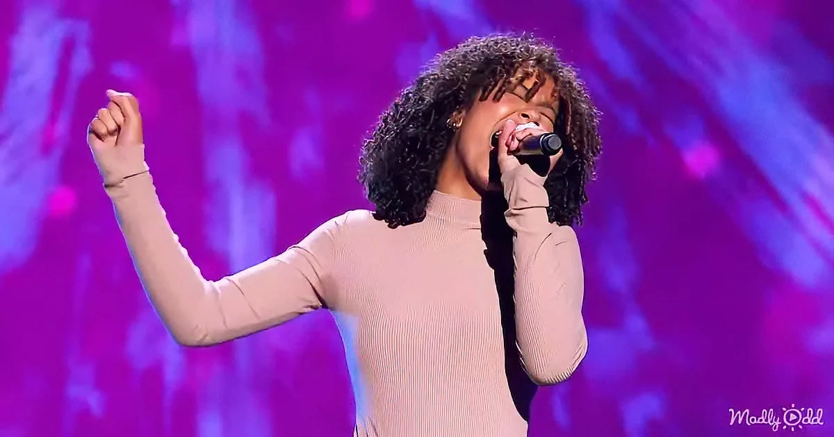 A person in a pink top sings passionately on stage with a microphone, surrounded by vibrant purple and blue lights.