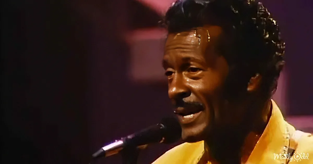 A man with curly hair and a yellow shirt sings into a microphone on stage.