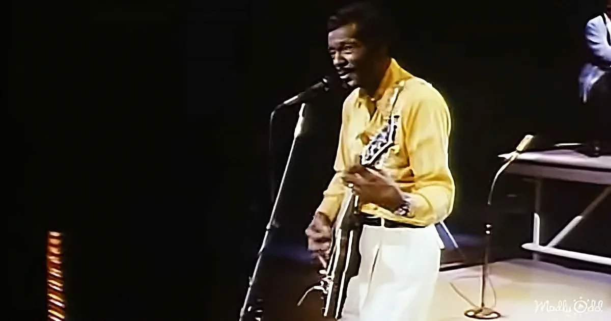 A man in a yellow shirt plays a saxophone on stage with a microphone in front of him.