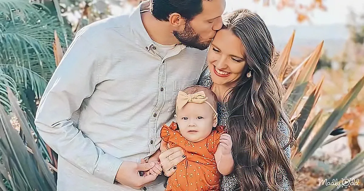A family of three, a man kissing a woman on the cheek, holding a baby in the center, surrounded by greenery.