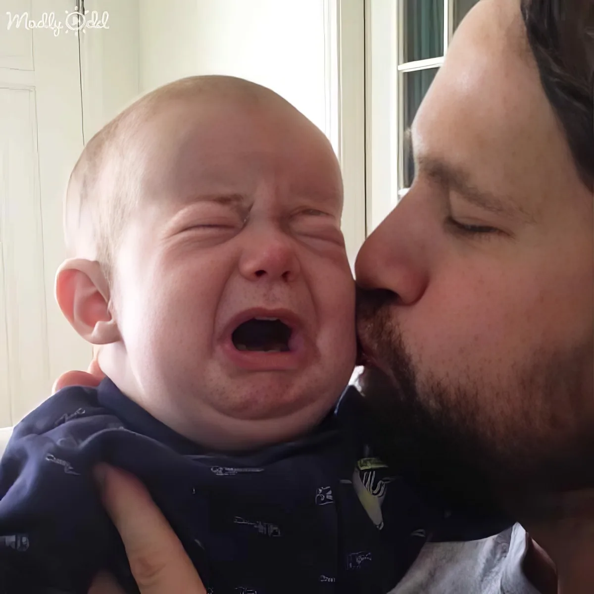 A man kisses a crying baby on the cheek, both appearing emotional.